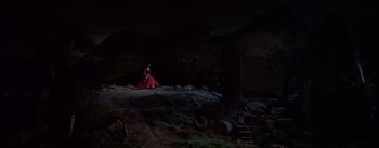 Movie still from “Brigadoon” (1954), directed by Vincente Minnelli – A woman in a long red dress sitting on top of a hill; Extreme Wide shot, High angle