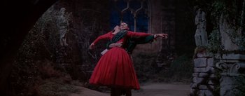 Movie still from “Brigadoon” (1954), directed by Vincente Minnelli – A man and a woman in a red dress dancing in front of a window at night; Wide shot, Low angle