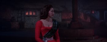 Movie still from “Brigadoon” (1954), directed by Vincente Minnelli – A woman in a red dress standing in front of a brick building; Medium shot, Over the shoulder angle