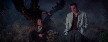 Movie still from “Brigadoon” (1954), directed by Vincente Minnelli – A man and a woman sitting next to each other in front of a tree; Medium shot, Low angle