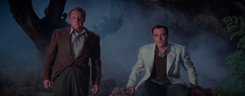 Movie still from “Brigadoon” (1954), directed by Vincente Minnelli – Two men are sitting in front of a smoke filled sky; Medium shot, Low angle