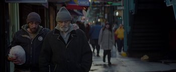 An older man walking down a street with people walking down the sidewalk