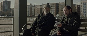 An older man sitting on a bench in front of some buildings