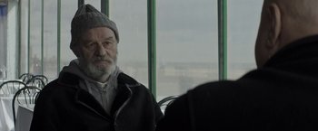 An older man sitting in front of a large window