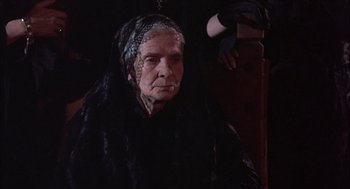 Movie still from “Bring Me the Head of Alfredo Garcia” (1974), directed by Sam Peckinpah – An old woman in a black dress and black gloves; Close Up shot, Over the shoulder angle