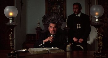 Movie still from “Bring Me the Head of Alfredo Garcia” (1974), directed by Sam Peckinpah – A man sitting at a table in front of a stack of papers; Medium shot, Low angle
