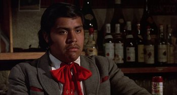 Movie still from “Bring Me the Head of Alfredo Garcia” (1974), directed by Sam Peckinpah – A man in a suit and red bow tie sitting in front of a bar; Close Up shot, Low angle