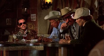 Movie still from “Bring Me the Head of Alfredo Garcia” (1974), directed by Sam Peckinpah – A group of men sitting at a bar drinking wine; Medium shot, Low angle