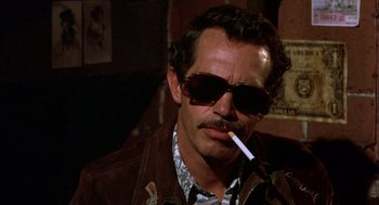 Movie still from “Bring Me the Head of Alfredo Garcia” (1974), directed by Sam Peckinpah – A man wearing sunglasses and holding a cigarette in his mouth; Close Up shot, Low angle