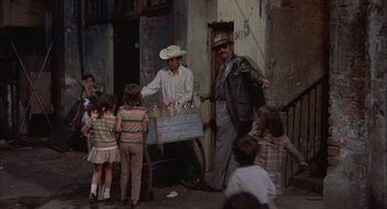 Movie still from “Bring Me the Head of Alfredo Garcia” (1974), directed by Sam Peckinpah – A group of children standing around a man selling drinks; Wide shot, High angle