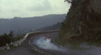 Movie still from “Bring Me the Head of Alfredo Garcia” (1974), directed by Sam Peckinpah – A car driving down a curvy road on a cloudy day; Extreme Wide shot, High angle