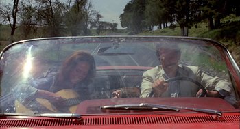 Movie still from “Bring Me the Head of Alfredo Garcia” (1974), directed by Sam Peckinpah – A man and a woman in a car with a guitar; Wide shot, High angle