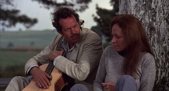 Movie still from “Bring Me the Head of Alfredo Garcia” (1974), directed by Sam Peckinpah – A man and a woman sitting next to each other with a guitar; Medium shot, Over the shoulder angle