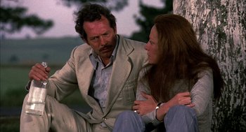 Movie still from “Bring Me the Head of Alfredo Garcia” (1974), directed by Sam Peckinpah – A man and a woman sitting next to each other on the ground; Medium shot, Low angle