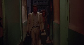 Movie still from “Bring Me the Head of Alfredo Garcia” (1974), directed by Sam Peckinpah – A man and a woman walking down a hall way holding suitcases; Wide shot, Low angle