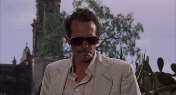 Movie still from “Bring Me the Head of Alfredo Garcia” (1974), directed by Sam Peckinpah – A man in a suit and sunglasses smoking a cigarette; Close Up shot, Low angle