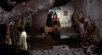 Movie still from “Bring Me the Head of Alfredo Garcia” (1974), directed by Sam Peckinpah – A woman standing in a room with a guitar in her hand; Wide shot, High angle