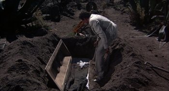 Movie still from “Bring Me the Head of Alfredo Garcia” (1974), directed by Sam Peckinpah – A man standing over an open casket in the dirt; Wide shot, High angle