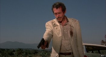 Movie still from “Bring Me the Head of Alfredo Garcia” (1974), directed by Sam Peckinpah – A man in a white jacket holding a gun in his hand; Medium shot, Low angle