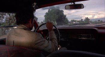 Movie still from “Bring Me the Head of Alfredo Garcia” (1974), directed by Sam Peckinpah – A man sitting in the driver's seat of a red car; Wide shot, Low angle