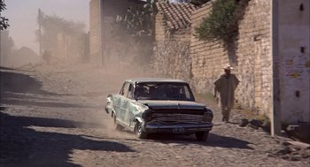 Movie still from “Bring Me the Head of Alfredo Garcia” (1974), directed by Sam Peckinpah – An old car driving down a dirt road; Wide shot, Low angle