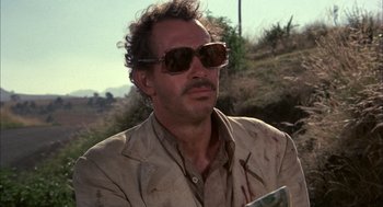 Movie still from “Bring Me the Head of Alfredo Garcia” (1974), directed by Sam Peckinpah – A man wearing sunglasses and a tan jacket; Close Up shot, Low angle