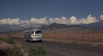 Movie still from “Bring Me the Head of Alfredo Garcia” (1974), directed by Sam Peckinpah – A bus driving down a dirt road near a field; Extreme Wide shot, Low angle