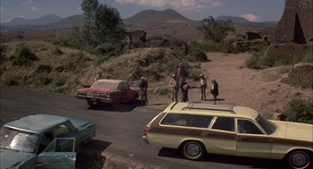 Movie still from “Bring Me the Head of Alfredo Garcia” (1974), directed by Sam Peckinpah – A group of people standing next to a car on the side of a road; Wide shot, High angle