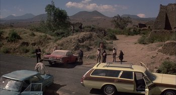 Movie still from “Bring Me the Head of Alfredo Garcia” (1974), directed by Sam Peckinpah – A group of people standing next to cars on a dirt road; Extreme Wide shot, High angle