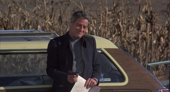 Movie still from “Bring Me the Head of Alfredo Garcia” (1974), directed by Sam Peckinpah – A man standing next to a car in front of a cornfield; Medium shot, Over the shoulder angle