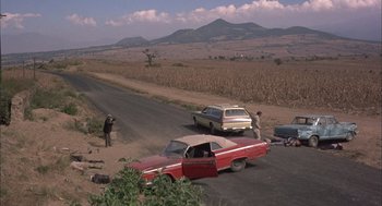 Movie still from “Bring Me the Head of Alfredo Garcia” (1974), directed by Sam Peckinpah – A man taking a picture of two cars on the side of the road; Extreme Wide shot, High angle