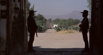 Movie still from “Bring Me the Head of Alfredo Garcia” (1974), directed by Sam Peckinpah – A man standing on the side of a road holding a rifle; Wide shot, Low angle