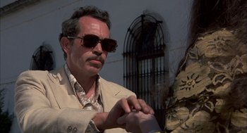 Movie still from “Bring Me the Head of Alfredo Garcia” (1974), directed by Sam Peckinpah – A man in a tan jacket and sunglasses looking at his watch; Close Up shot, Low angle
