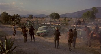 Movie still from “Bring Me the Head of Alfredo Garcia” (1974), directed by Sam Peckinpah – A group of people standing on a dirt road near a car; Extreme Wide shot, High angle