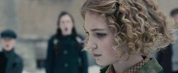Movie still from “The Book Thief” (2013), directed by Brian Percival – A young girl with curly blonde hair looking at the camera while a young woman stands in the background; Close Up shot, Over the shoulder angle