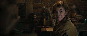 Movie still from “The Book Thief” (2013), directed by Brian Percival – A girl is smiling for the camera in a room with a brick wall; Close Up shot, High angle