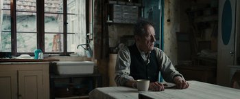 Movie still from “The Book Thief” (2013), directed by Brian Percival – An older man sitting at a table with a cup of coffee; Medium shot, Over the shoulder angle