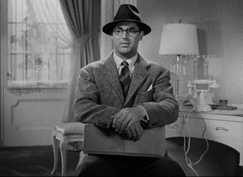 Movie still from “Bringing Up Baby” (1938), directed by Howard Hawks – A man sitting in a chair wearing a suit and hat; Medium shot, Over the shoulder angle