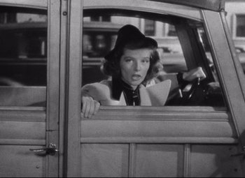Movie still from “Bringing Up Baby” (1938), directed by Howard Hawks – A black and white photo of a woman driving a car; Medium shot, Low angle