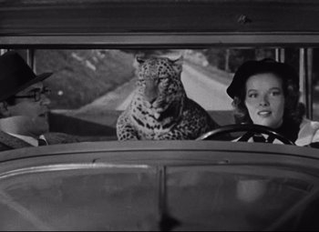 Movie still from “Bringing Up Baby” (1938), directed by Howard Hawks – Two women and a man in a car with a leopard in the window; Medium shot, Over the shoulder angle