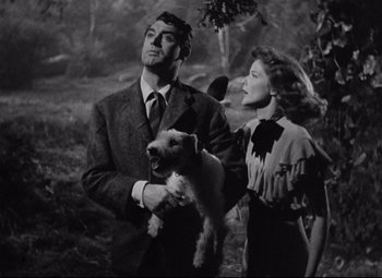 Movie still from “Bringing Up Baby” (1938), directed by Howard Hawks – A man and woman holding a dog in a forest; Medium shot, Low angle