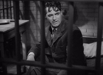 Movie still from “Bringing Up Baby” (1938), directed by Howard Hawks – A man sitting in front of a brick wall behind bars; Medium shot, Over the shoulder angle