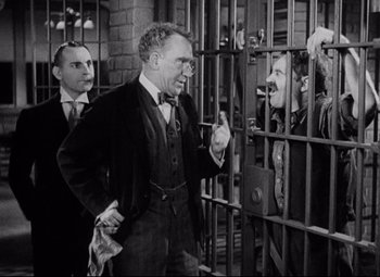 Movie still from “Bringing Up Baby” (1938), directed by Howard Hawks – A man in a suit talking to a man in a jail cell; Medium shot, Over the shoulder angle