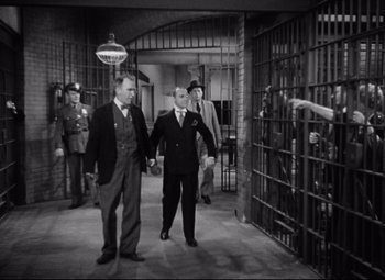Movie still from “Bringing Up Baby” (1938), directed by Howard Hawks – A group of men in suits walking through a jail cell; Wide shot, High angle