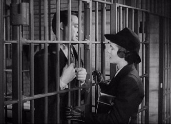 Movie still from “Bringing Up Baby” (1938), directed by Howard Hawks – A man and a woman are standing next to each other in front of bars; Medium shot, High angle