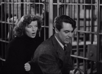 Movie still from “Bringing Up Baby” (1938), directed by Howard Hawks – A man and a woman standing next to each other in front of a cage; Medium shot, Low angle