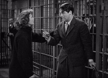 Movie still from “Bringing Up Baby” (1938), directed by Howard Hawks – A man and a woman are holding hands in a jail cell; Medium shot, Over the shoulder angle