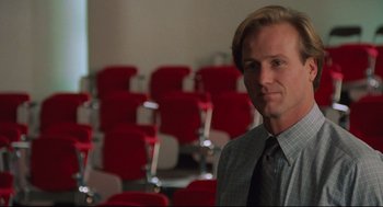 Movie still from “Broadcast News” (1987), directed by James L. Brooks – A man standing in front of red chairs in a room; Close Up shot, Low angle
