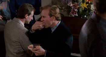 Movie still from “Broadcast News” (1987), directed by James L. Brooks – A man eating a hot dog while another man looks on; Medium shot, Over the shoulder angle