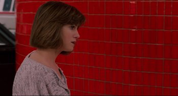Movie still from “Broadcast News” (1987), directed by James L. Brooks – A woman with short brown hair standing in front of a red wall; Medium shot, Over the shoulder angle